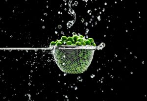 Article: Companion plants for Peas. A Small strainer with peas and water splashes on a black background