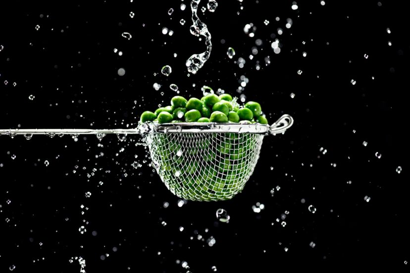 A Small strainer with peas and water splashes on a black background