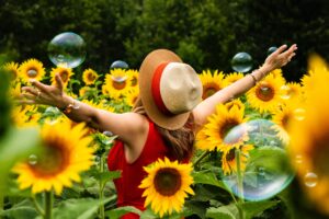 Field f Sunflowers with a lady dressed in red standing facing the sun with her arms outstretched in the air straw hat with a red ribbon very pretty