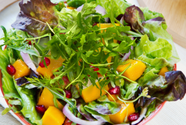 A vibrant bowl of mixed leaf salad featuring fresh arugula, colorful lettuce, succulent mango chunks, and juicy pomegranate seeds.