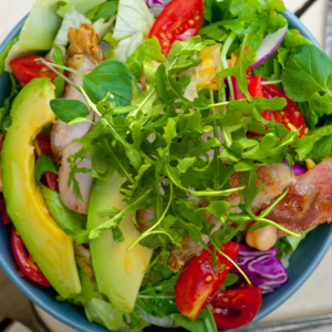 Article: Arugala Companion Plants. Pic - Gourmet salad with arugula, avocado slices, crispy bacon, cherry tomatoes, and red onions, offering a feast of flavors and textures.