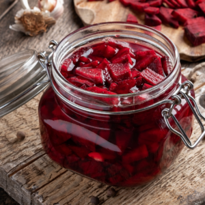 : A jar of pickled beets cut into cubes on a rustic wooden table, surrounded by beet pieces and spices.