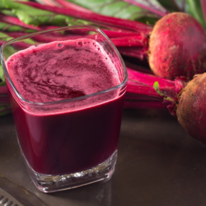 "Glass of fresh beet juice and beets on a bench."