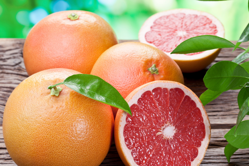 Whole and halved grapefruits with rich, ruby-red flesh and green leaves, resting on a wooden surface.