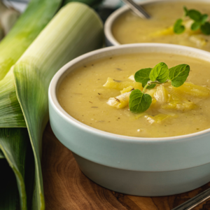 A bowl of creamy leek soup garnished with fresh herbs, accompanied by whole leeks, symbolizing home-cooked warmth.