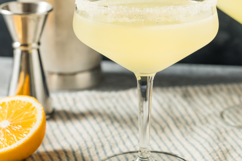 A chilled margarita cocktail with a salted rim, garnished with a lemon wedge on a glass table."