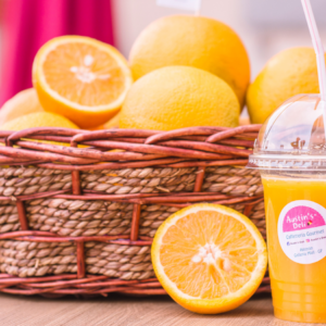  A basket of fresh oranges with a halved orange in front, next to a cup of orange juice.