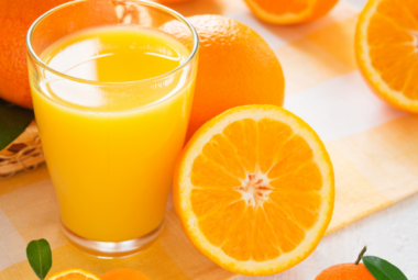 A refreshing glass of orange juice surrounded by whole and halved oranges on a sunny table.