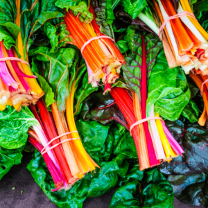 "Bundles of Swiss chard with bright red, orange, and yellow stems arranged on dark green leaves."