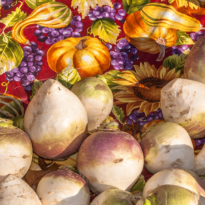 A pile of turnips on a decorative autumn-themed tablecloth featuring illustrations of pumpkins, grapes, and sunflowers.