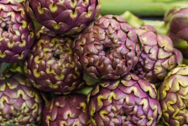 "Close-up of a pile of vibrant purple artichokes with green highlights, freshly harvested and displayed at a market."