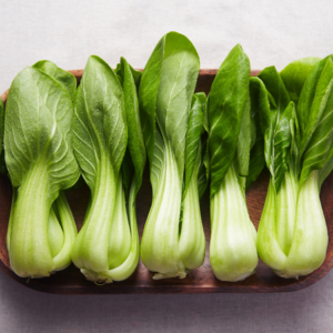 Fresh bok choy neatly lined up on a wooden tray, with crisp green leaves and white stalks.
