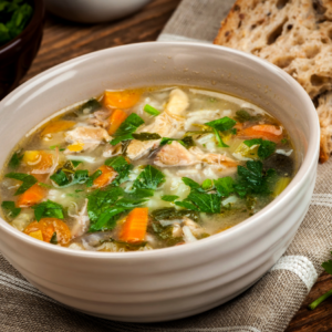 A bowl of hearty vegetable soup with chunks of chicken and fresh garden greens, served with a side of whole grain bread.