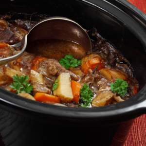 A steaming crockpot filled with a hearty winter soup, garnished with fresh parsley, featuring tender meat, carrots, and potatoes.