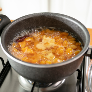  Apricot compote simmering in a grey pot on a stove, with bubbling fruit pieces visible.