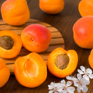 Whole and halved apricots on a wooden cutting board, decorated with apricot blossoms.