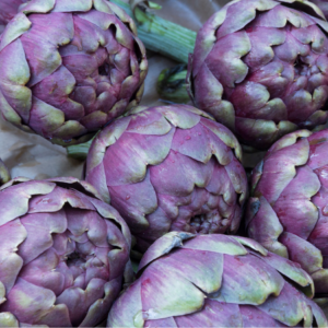 Article: Artichoke Companion Plants. Pic - Close-up of fresh, raw artichokes with vibrant purple and green leaves, lightly sprinkled with water droplets.