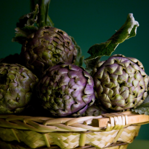 Article: Artichoke Companion Plants. Pic - A basket of deep purple artichokes against a dark green background, highlighting their intricate textures and rich colors.