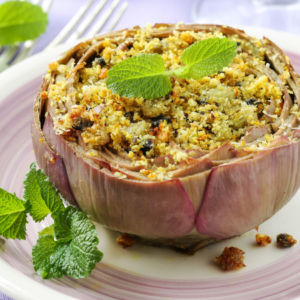 Article: Artichoke Companion Plants. Pic - A whole roasted artichoke filled with a golden breadcrumb stuffing, garnished with fresh mint leaves on a decorative plate.