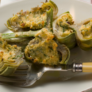 Article: Artichoke Companion Plants. Pic - Sliced artichokes stuffed with a herbed breadcrumb mixture on a white plate, accompanied by a vintage fork.