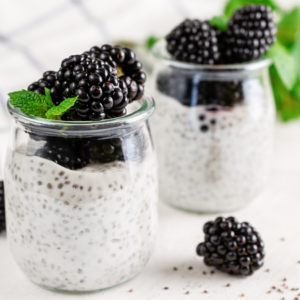 Article:Blackberry Companion Plants. Pic - Two jars of chia pudding topped with fresh blackberries and mint leaves on a white wooden table.
