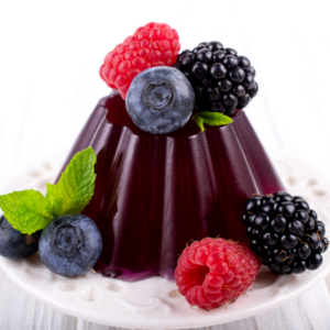 A glossy berry jelly dessert adorned with blackberries, blueberries, raspberries, and mint leaves on a white plate.