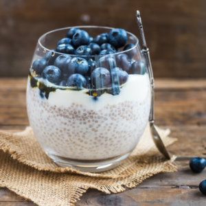 Article: Companion Planting Blueberries. Pic -A glass of chia seed pudding topped with a layer of yogurt and fresh blueberries, on a rustic wooden table.