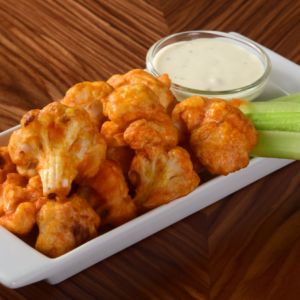 Article: Cauliflower companion planting. Pic - Buffalo cauliflower bites served in a white dish with a side of celery sticks and ranch dipping sauce.