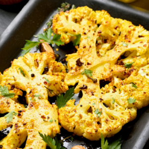 Roasted cauliflower steaks with turmeric and spices, garnished with fresh herbs, on a baking tray.