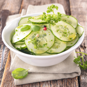 A fresh cucumber salad garnished with herbs and colorful peppercorns in a white bowl.