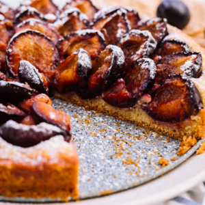 Close-up of a fig tart with a slice removed, showing the juicy fig filling and dusted with powdered sugar.