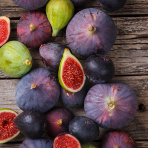 Various ripe and unripe figs, some cut open to reveal their red interiors, arranged on a rustic wooden surface.