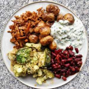 A plate of roasted baby potatoes, tzatziki sauce, red kidney beans, cooked broccoli, and shredded seasoned meat, arranged in separate sections.