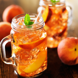 Article : Growing Peach Trees in Pots. Pic - Two mason jars filled with iced peach tea, garnished with peach slices and fresh mint, with whole peaches in the background.