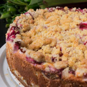 Article: Rhubarb Companion Plants. Pic - Close-up of a whole rhubarb crumble pie on a plate, showcasing its golden crumbly topping and pink rhubarb filling.