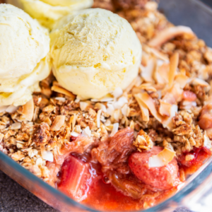  A bowl of rhubarb crumble topped with three scoops of vanilla ice cream and sprinkled with toasted coconut flakes.