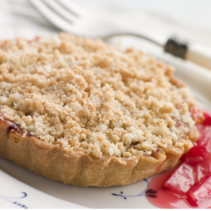 Article: Rhubarb Companion Plants. Pic - Close-up of a rhubarb crumble pie on a plate with a fork.