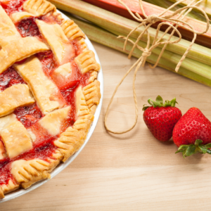 Freshly baked rhubarb pie with a lattice crust alongside raw rhubarb stalks and strawberries.