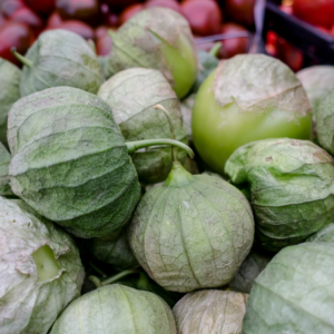 Article: Tomatillo Companion Plants . Pic - Companion "Close-up of a group of green tomatillos, each encased in its natural husk, displayed among other vegetables at a market."