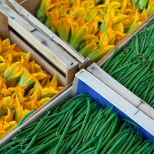 Article; Grow Your Own Low-Oxalate Foods. Pic - Wooden crates filled with fresh green beans and bright yellow zucchini flowers at a market.
