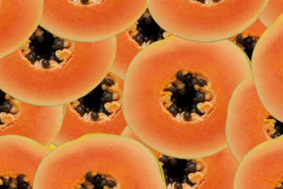Multiple slices of papaya with orange flesh and black seeds arranged in an overlapping pattern.